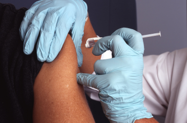 A medical professional with latex gloves on administers a vaccine into the arm of a patient