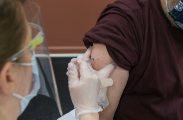 Medical professional wearing a mask and a face shield administers a vaccine into a patient's arm