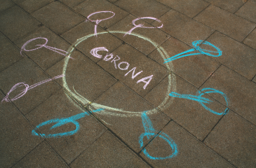 The word CORONA written in chalk on a sidewalk with a circle around it and several circles drawn out from it like a network
