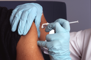 A medical professional with blue gloves administers a vaccine into the arm of a patient