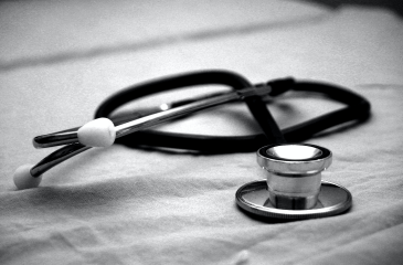 Black and white photo of a stethoscope draped on a hospital bed