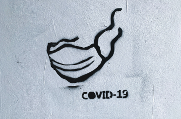 Graffiti stencil of a mask with the word COVID-19 below it
