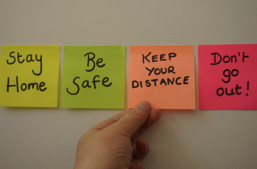 Post-it notes of different colors in a horizontal line reading "Stay home" "Be safe" "Keep your distance" "Don't go out!"