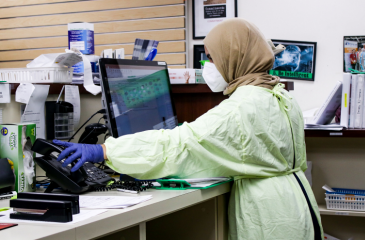 Lap worker in a hijab, lab protective gear, and mask working at a computer