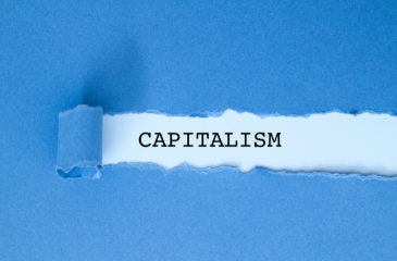 A blue piece of paper torn off revealing the word "capitalism" behind it