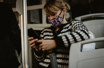 A woman in a mask on a bus looking at her phone