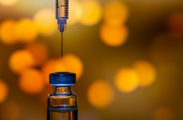 A syringe about to enter a bottle of vaccine