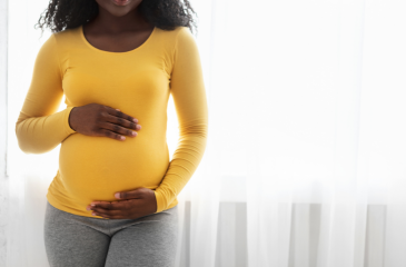 Black pregnant person in a yellow shirt holding her stomach