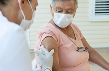 An elderly person in a mask receiving a vaccine in the arm by a medical professional in a mask