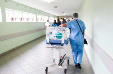 Health professional walking down a hallways with an infant on a hospital NICU bed