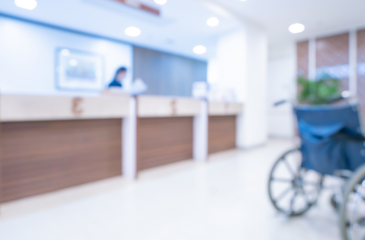 Blurred image of a hospital reception desk and a patient in a wheelchair