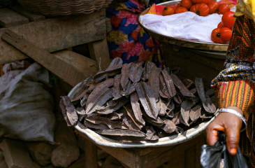 Tamarind pods in a bowl along with red vegetables and the hand of a merchant. Shot at a market in Ghana.