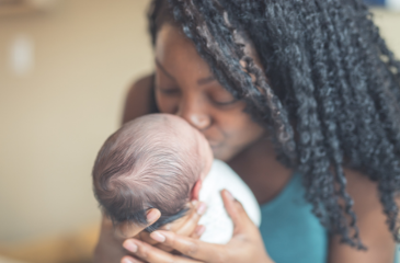 Black mother holds infant and kisses their face