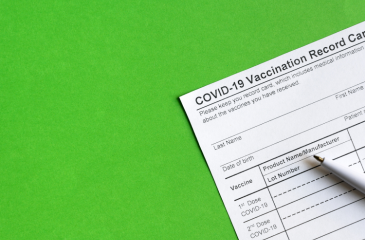 A COVID-19 Vaccine Record card with a pen laid across a green backdrop