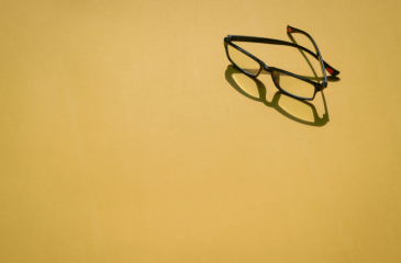 A pair of glasses with a forward shadow on a yellow background