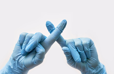 Two hands in blue latex gloves with their pointer fingers crossed signaling "No"