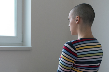 Young woman with shaved head from chemotherapy looking blankly out a window