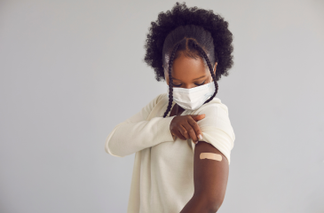 Young woman of color pulling up her sleeve to show a bandaid where she was vaccinated