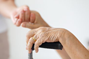 Hands of an elderly person resting on a cane with their other hand held by a younger person