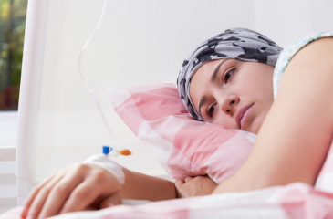 Adolescent with chemo hat and IV staring into the distance while laying in bed