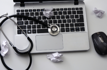 Open laptop with a mouse, stethoscope, and crumpled notes